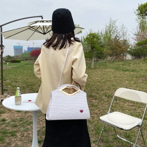Vue détaillée du sac blanc à motif crocodile avec poignée en métal dorée en forme de lèvres