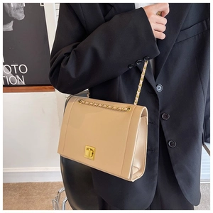 Sac bandoulière beige rectangulaire avec chaîne dorée porté sur blazer noir