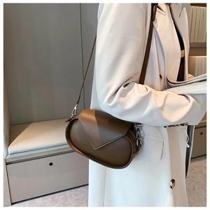 Close-up of a brown leather shoulder bag with V-shaped flap on a beige coat