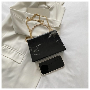 Close-up of black marble acrylic box bag with golden bamboo handle and chain strap