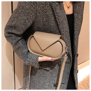 Detail of khaki leather crossbody bag with triangle flap and silver hardware on a model