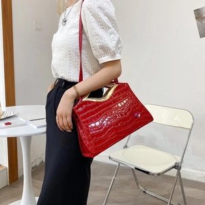 Détail du sac rouge en similicuir crocodile avec poignée en métal doré sur table