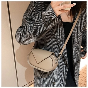 Mirror selfie showing the beige crossbody bag with V-shaped flap on an overcoat