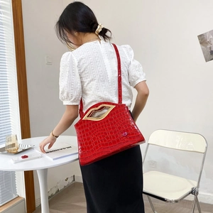 Détail d'un sac à main rouge effet crocodile avec une poignée dorée en forme de lèvres