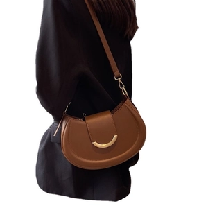 Brown semi-circle crossbody saddle bag with gold hardware shown on model with white background