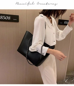 Close-up of black leather tote bag with metal chain strap worn as a crossbody bag