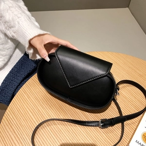 Detail of a minimalist black oval crossbody bag with triangle flap on a wooden surface
