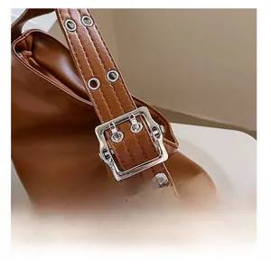 Détail rapproché de la bandoulière en similicuir marron avec œillets argentés et boucle