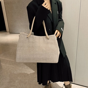 Large beige woven canvas tote bag with thick rope handles shown on a model