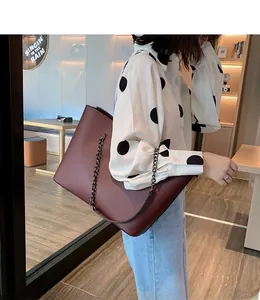 Close-up of a large burgundy tote bag with gun-black metal chain strap shown on shoulder