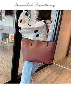 Detail of dark reddish-brown tote bag with metal chain strap worn by a model in a hotel