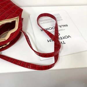 Détail d'un sac à main rouge texturé crocodile avec un fermoir doré en forme de lèvres