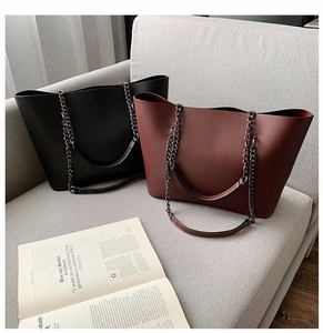 Detail of minimalist tote bags in black and burgundy with chain straps on a sofa
