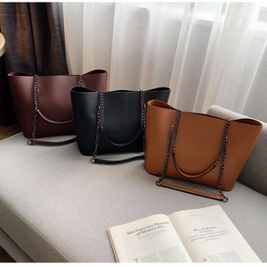Three leather tote bags in burgundy, black and caramel colors on a soft gray sofa
