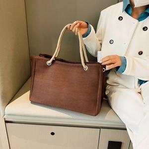 Detail of dark brown canvas straw tote bag with beige rope handles and metal D-rings