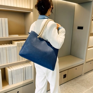 Blue canvas tote bag with thick rope handles shown on shoulder in a minimalist setting