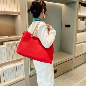 Detailed view of red canvas tote bag with woven rope handles worn on shoulder