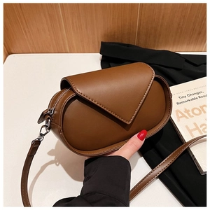 Brown oval crossbody bag with triangular flap and stitching detail on wooden background