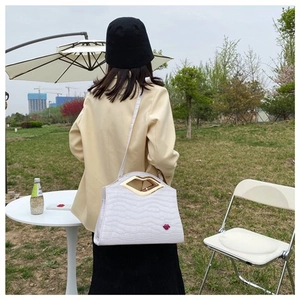 Sac à main blanc en cuir ondulé avec poignée dorée en forme de lèvres et badge rouge