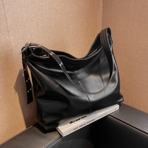 Détail du sac hobo noir brillant sur des livres blancs avec garniture en anneaux argentés