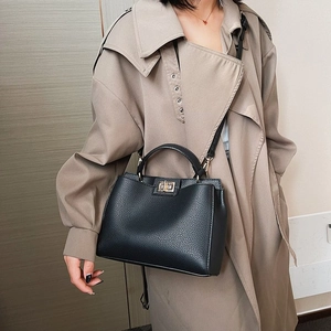 Borsa a mano nera in pelle a grana con fibbia dorata abbinata a un classico trench
