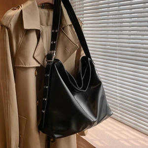 Détail du sac hobo en similicuir noir avec œillets argentés sur la large bandoulière