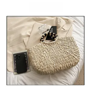 Detail of woven straw handbag featuring vintage wooden bead handle on neutral background