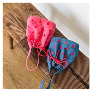 Pink velvet and blue denim drawstring mini bags with red heart patterns on a wooden bench