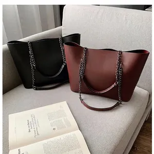 Classic black and burgundy leather tote bags with metal chain straps on a modern sofa