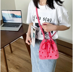Hot pink bucket bag with red heart embroidery and drawstring closure on a female model