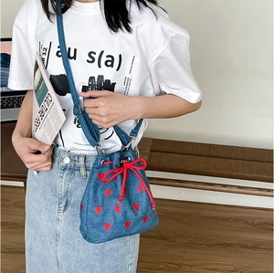 Detail of blue denim bucket bag with red heart embroidery and matching drawstring cord