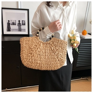 Detail of hand-woven straw handbag featuring chic wooden bead handle and crescent shape