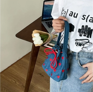 Blue denim bucket bag with red heart embroidery and drawstring closure in a lifestyle setting