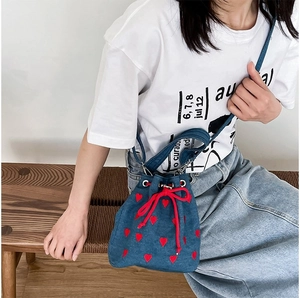 Detail of blue denim bucket bag with red heart embroidery and drawstring closure