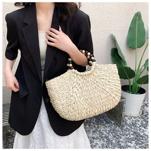 Detail of cream woven handbag featuring decorative tri-color wooden bead handle and texture