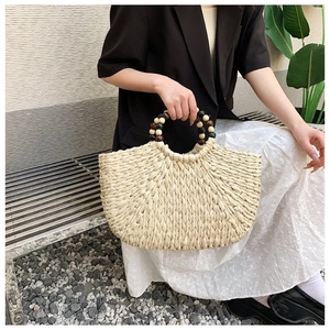 Detail of woven straw handbag with decorative wooden beads on modern metal bench