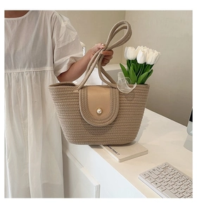 Détail du sac cabas en paille avec rabat en cuir beige et fermoir perle sur table