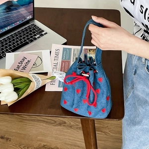 Denim bucket bag with red heart embroidery and drawstring closure in a lifestyle setting