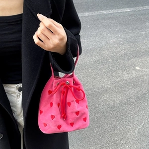 Pink drawstring bucket bag with red heart embroidery held by a model on a street background