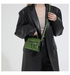 Dettaglio di una borsa in pelle verde scuro abbinata a un blazer chic in pelle nera oversize