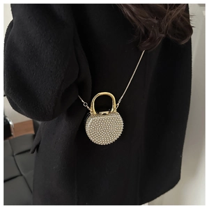 Detailed view of a golden circular evening bag with pearls and chain on a black coat