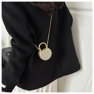 Detail of a round gold mini bag with beaded texture and metal ring handle on a model