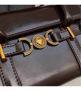 Vue détaillée de la boucle cœur dorée et du cuir marron sur le sac à bandoulière