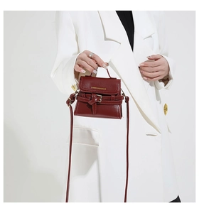 Dettaglio mini borsa a tracolla bordeaux con scritte dorate su un blazer bianco