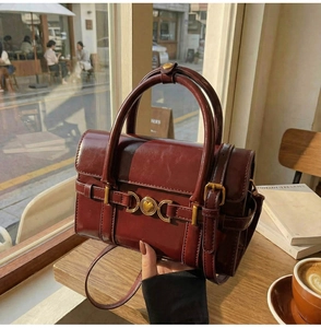 Détail du sac bandoulière vintage bordeaux avec ornements dorés en forme de cœur sur une table