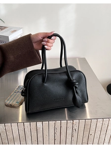 Détail du sac Boston noir en cuir grainé avec poignée nouée et logo minimaliste