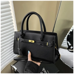 Detail of black lychee grain leather bag with gold hardware lock and strap handles