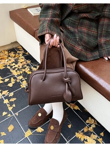 Détail du sac à main en cuir marron à motif litchi avec texte gaufré et breloque feuille