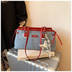 Detail of denim crossbody bag featuring red leather trim and silver star metal pendant