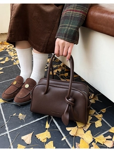 Détail du sac à main en cuir grainé marron foncé avec sangle nouée sur fond de feuilles d'automne